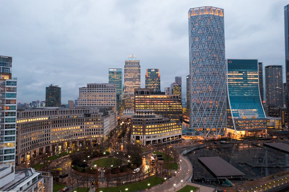 A modern high-rise office building with a predominantly glass facade reflecting the blue sky is visible in the image. The structure features curved and angular glass panels, with horizontal and vertic